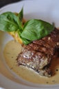 Delicious grilled beef steak on a white plate with brown sauce and some basil leaves as decoration. Tasty lunch or dinner at a