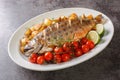 Delicious healthy grilled whole fish arctic char served with fried potatoes, cherry tomatoes and lime close-up on a dish.