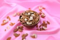 Delicious and healthy mixed dried fruit, nuts and seeds in a wooden bowl on pink silky background