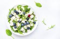 Delicious healthy salad with sweet melon, red onion, feta cheese, blueberries, arugula and mixed herbs, white table background, Royalty Free Stock Photo