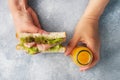 Delicious healthy sandwich for a snack breakfast in women hands. Toast bread tomato ham leaf salad, juice in a bottle Royalty Free Stock Photo