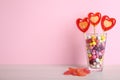 Delicious heart shaped lollipops, dragees and jelly candies on table against pink background. Space for text