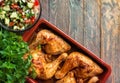 Delicious home cooked baked chicken thighs with herbs onion garlic in Mediterranean style in clay dish tomatoes cucumber parsley Royalty Free Stock Photo