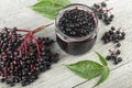 Delicious homemade black elderberry syrup in glass jar and bunches of black elderberry with green leaves on wooden desk