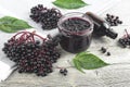 Delicious homemade black elderberry syrup in glass jar and bunches of black elderberry with green leaves on wooden desk
