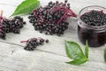 Delicious homemade black elderberry syrup in glass jar and bunches of black elderberry with green leaves on wooden desk