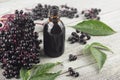 Delicious homemade black elderberry syrup in glass jar and bunches of black elderberry with green leaves on wooden desk