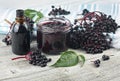 Delicious homemade black elderberry syrup in glass jar and bunches of black elderberry with green leaves on wooden desk.