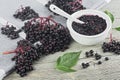 Delicious homemade black elderberry syrup in glass jar and bunches of black elderberry with green leaves on wooden desk.