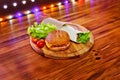 Delicious homemade burger with tomatoes, cheese, cucumber and lettuce leaves on a wooden background and lights on the background Royalty Free Stock Photo