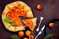 Delicious French galette with apricots and mint with cut piece. Traditional biscuit on black plate, fork and knife on dark grunge