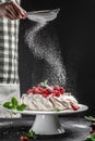 Delicious homemade Pavlova cake with fresh strawberries and whipped cream. chef hands with powder in a freeze motion of a cloud of