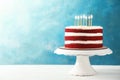 Delicious homemade red velvet cake with candles on table against color background. Royalty Free Stock Photo