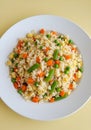 A white plate filled with fried rice with peas carrots and green beans on a yellow background table top Royalty Free Stock Photo