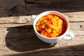 Delicious juicy appetizer of stewed vegetables in white bowl on old wooden table. Rustic style. Sunlight and sharp shadows.