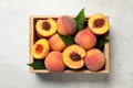 Delicious juicy peaches and leaves in crate on light grey textured table, top view Royalty Free Stock Photo