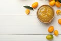 Delicious kumquat jam in bowl and fresh fruits on white wooden table, flat lay. Space for text Royalty Free Stock Photo