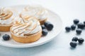 Delicious lemon tartlets with meringue on a white vintage plate. Sweet treat on a light blue background Royalty Free Stock Photo