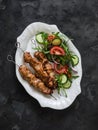 Delicious lunch, appetizer, tapas - chicken skewers and fresh vegetable salad on a dark background, top view