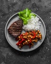 Delicious lunch - grilled steak, rice and roasted eggplant, pepper, chickpeas stew on a dark background, top view