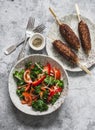 Delicious lunch - kale, tomatoes, sweet pepper salad and kebabs on a gray background, top view Royalty Free Stock Photo