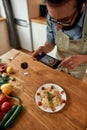 Delicious meal. Young man, cook taking picture of garlic butter shrimp pasta, meal decorated with basil and cherry