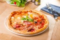 Delicious Meat Pizza with bacon and sausages on white plate on the wooden table with cutlery and ingredients. Selective focus, Royalty Free Stock Photo