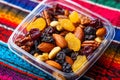 Delicious mixed nuts and dried fruit in transparent container on colorful textile Royalty Free Stock Photo