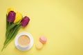 Delicious morning coffee, macarons and flowers on yellow background, flat lay. Space for text