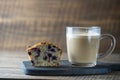 Delicious muffin with blueberries and cappuccino glass cup on wooden table, closeup. Fresh cupcake and coffee for breakfast