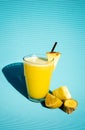 Delicious natural pineapple juice inside a glass with pieces of pineapple on one side on a blue table