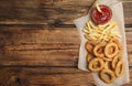 Delicious onion rings, fries and ketchup on wooden table, top view. Space for text Royalty Free Stock Photo