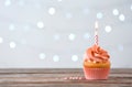 Delicious orange cupcake with burning candle on table against blurred background.