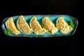 Delicious pan fried Asian gyoza stuffed with meat, served on a blue plate. Japanese Jiaozi or dumplings isolated on black