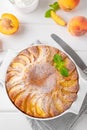 Delicious peach pie in a white ceramic baking form on a white wooden background. Summer cake. Selective focus, copy space Royalty Free Stock Photo