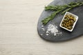 Delicious pickled capers, salt and rosemary twigs on white wooden table, top view. Space for text Royalty Free Stock Photo