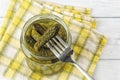 Delicious pickled cornichon on a fork over full glass jar against checkered napkin on a table. Whole green gherkins marinated with Royalty Free Stock Photo