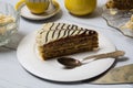 Delicious piece of cake with cream  nuts and chocolate close-up on a white plate  coffee in a yellow cup on a light wooden table Royalty Free Stock Photo