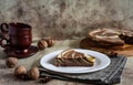 A delicious piece of cake on a white plate and a striped chocolate cake on a wooden platter on a gray background