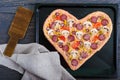 Delicious pizza in a heart shape, ready for baking. Pizza with mushrooms, salami, pepperoni, olives, corn on a baking tray. Royalty Free Stock Photo