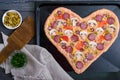 Delicious pizza in a heart shape, ready for baking. Pizza with mushrooms, salami, pepperoni, olives, corn on a baking tray. Royalty Free Stock Photo