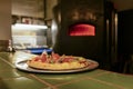 Delicious pizza served on metal plate over professional open kitchen in restaurant, fireplace stove on the background