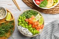 Delicious poke bowls with fish and edamame beans on white wooden table, flat lay