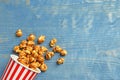 Delicious popcorn with caramel in paper bucket on wooden background, top view