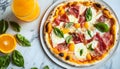 Delicious prosciutto pizza with mozzarella and basil, served with refreshing orange drinks on marble table Royalty Free Stock Photo