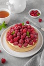 Delicious raspberry tart with vanilla custard cream sprinkled with powdered sugar on a white plate on a gray concrete background. Royalty Free Stock Photo