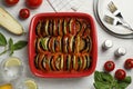 Delicious ratatouille in baking dish and ingredients on white wooden table, flat lay Royalty Free Stock Photo