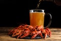 Delicious red boiled crayfishes and pouring beer into mug on wooden table