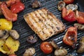 Delicious salmon and vegetables on the grill. Close-up on grilling square shape salmon, red and yellow peppers, cherry tomatoes Royalty Free Stock Photo