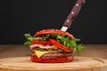 Delicious red spicy burger with beef patty, bun and sorcery and chilli on a serving wooden board with a stuck knife on a